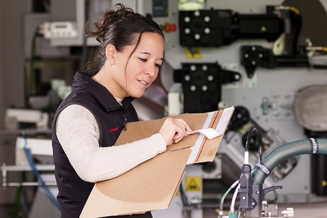 Woman inspecting the silicone release liners and tear strips applied by Robatech’s Vivo 18 coating head on a corrugated board